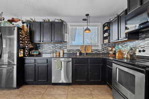 Kitchen featuring appliances with stainless steel finishes, a textured ceiling, tasteful backsplash, light tile patterned floors, and decorative light fixtures