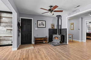 Foyer featuring ceiling fan, a wood stove, wood finished floors, and a textured ceiling