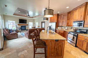 Kitchen with stainless steel appliances, a ceiling fan, stone tile floors, a center island with sink, and recessed lighting