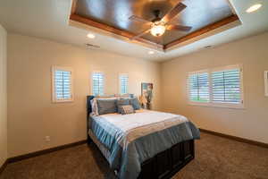 Bedroom featuring a tray ceiling, dark carpet, multiple windows, recessed lighting, and ceiling fan