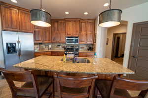 Kitchen with appliances with stainless steel finishes, brown cabinets, tasteful backsplash, light stone counters, and recessed lighting