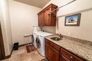 Laundry area with cabinet space, washer and clothes dryer, and light stone finish floors
