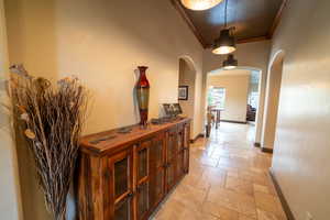 Hall featuring stone tile flooring, arched walkways, and crown molding