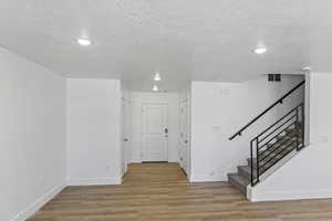 Corridor with a textured ceiling, light wood finished floors, stairway, and recessed lighting