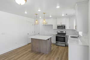Kitchen featuring stainless steel appliances, light wood-type flooring, tasteful backsplash, light countertops, and white cabinetry