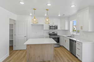 Kitchen with appliances with stainless steel finishes, tasteful backsplash, light wood-style floors, white cabinets, and recessed lighting