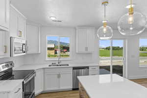 Kitchen with stainless steel appliances, light wood-type flooring, light countertops, white cabinets, and a textured ceiling