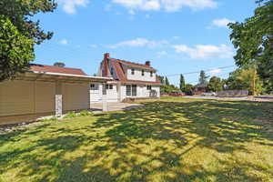Back of property with a chimney, a patio, a lawn, and a gambrel roof