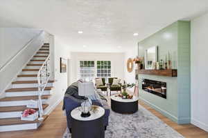 Living room with stairway, light wood-style flooring, a glass covered fireplace, a textured ceiling, and recessed lighting