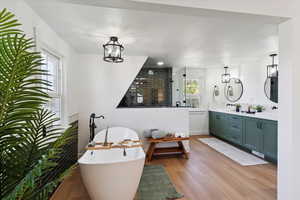 Bathroom with double vanity, wood finished floors, a freestanding bath, walk in shower, and a chandelier