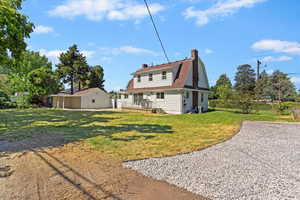Back of property featuring a chimney, a yard, and a gambrel roof