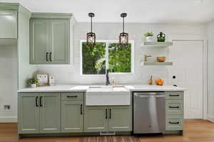Kitchen with green cabinetry, stainless steel dishwasher, open shelves, tasteful backsplash, and light wood-type flooring
