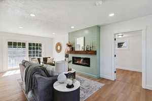 Living room featuring a large fireplace, plenty of natural light, light wood-style floors, a textured ceiling, and recessed lighting