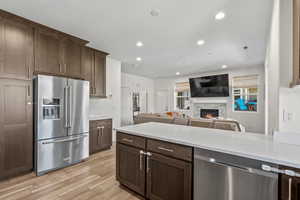 Kitchen featuring appliances with stainless steel finishes, a fireplace, light wood-style flooring, light countertops, and dark brown cabinetry