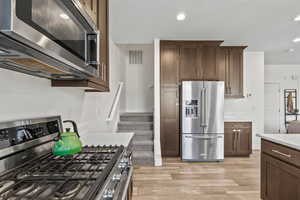 Kitchen with stainless steel appliances, light wood-style flooring, light countertops, dark brown cabinets, and recessed lighting
