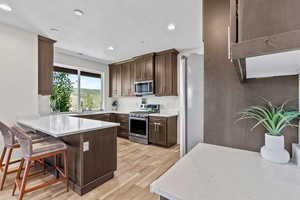 Kitchen with stainless steel appliances, light wood finished floors, a peninsula, light countertops, and a breakfast bar