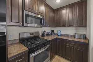 Kitchen with appliances with stainless steel finishes, dark brown cabinetry, and light tile patterned floors