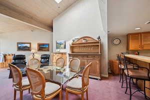 Carpeted dining area featuring a textured wall, wood ceiling, and vaulted ceiling