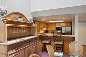 Kitchen featuring stainless steel refrigerator with ice dispenser, black microwave, a breakfast bar, light countertops, and recessed lighting