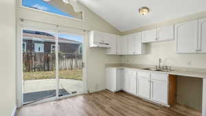 Kitchen with under cabinet range hood, white cabinetry, light wood-type flooring, ceiling fan, and high vaulted ceiling