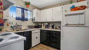 Kitchen featuring white appliances, white cabinets, light wood-style floors, dark cabinetry, and light countertops
