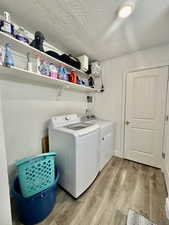 Laundry area with independent washer and dryer, light wood finished floors, and a textured ceiling