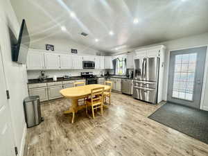 Kitchen with stainless steel appliances, dark countertops, recessed lighting, light wood-style flooring, and white cabinetry