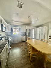 Kitchen with stainless steel appliances, a textured ceiling, dark countertops, dark wood finished floors, and white cabinets