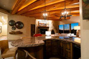 Kitchen with beam ceiling, a chandelier, open floor plan, decorative light fixtures, and stone counters