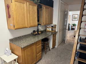 Kitchen with light carpet, built in study area, and dark stone countertops