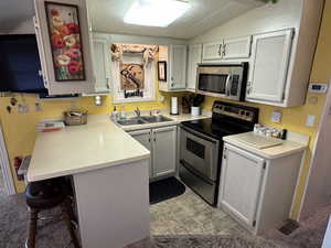 Kitchen featuring appliances with stainless steel finishes, a peninsula, light countertops, a breakfast bar, and vaulted ceiling
