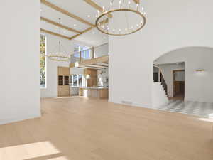 Unfurnished living room with a chandelier, light wood-style floors, stairway, beam ceiling, and a high ceiling