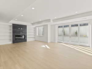 Unfurnished living room featuring recessed lighting, built in features, a large fireplace, light wood finished floors, and a raised ceiling