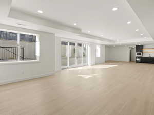 Unfurnished living room featuring a raised ceiling, recessed lighting, and light wood-style flooring