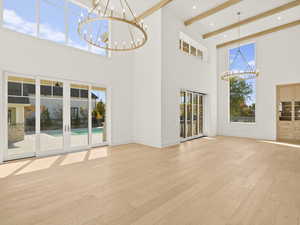 Unfurnished living room featuring a chandelier, light wood finished floors, beam ceiling, and a towering ceiling