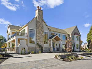 View of front facade featuring stone siding, a chimney, a shingled roof, and driveway