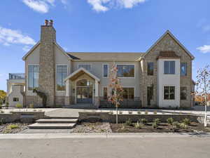 View of front facade with stone siding, a chimney, french doors, and roof with shingles