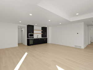 Unfurnished living room featuring light wood-style flooring, recessed lighting, and bar with sink