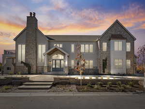 View of front of home featuring stone siding, a chimney, and roof with shingles
