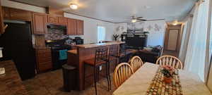 Kitchen featuring black appliances, under cabinet range hood, a kitchen bar, ceiling fan, and dark tile patterned flooring