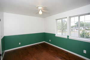 Spare room featuring healthy amount of natural light, a ceiling fan, dark wood-style floors, and a textured ceiling