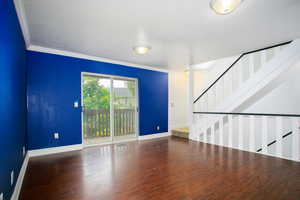 Unfurnished living room with wood finished floors, crown molding, and stairway