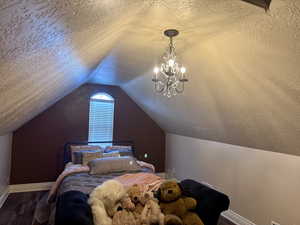 Bedroom with a textured ceiling, vaulted ceiling, wood finished floors, and a chandelier