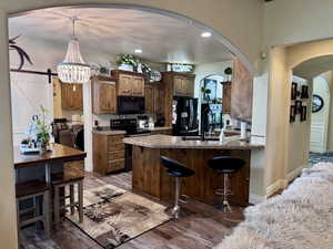 Kitchen with black appliances, arched walkways, a breakfast bar, wood finished floors, and recessed lighting