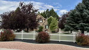 View of property hidden behind natural elements featuring stone siding and a fenced front yard