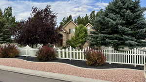 View of property hidden behind natural elements featuring stone siding, a fenced front yard, and stucco