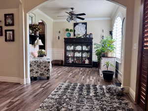 Sitting room with wood finished floors, a ceiling fan, arched walkways, crown molding, and wainscoting