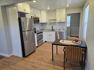 Kitchen with stainless steel appliances, open shelves, light wood-style flooring, white cabinetry, and light stone counters