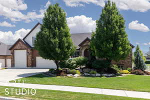 View of front facade with stone siding, a front lawn, concrete driveway, and a garage