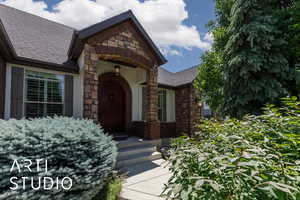 Entrance to property featuring roof with shingles, brick siding, and stone siding